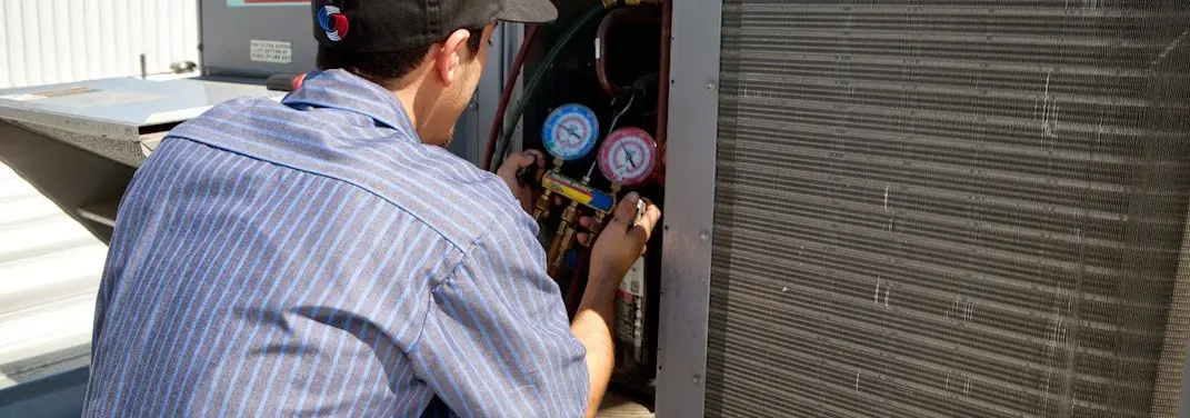 HVAC technician servicing a condenser unit in Plainview